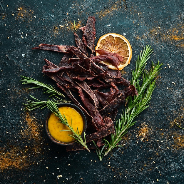 Jerky Dried meat slices with spices and herbs Snacks for beer On a black stone background Top view