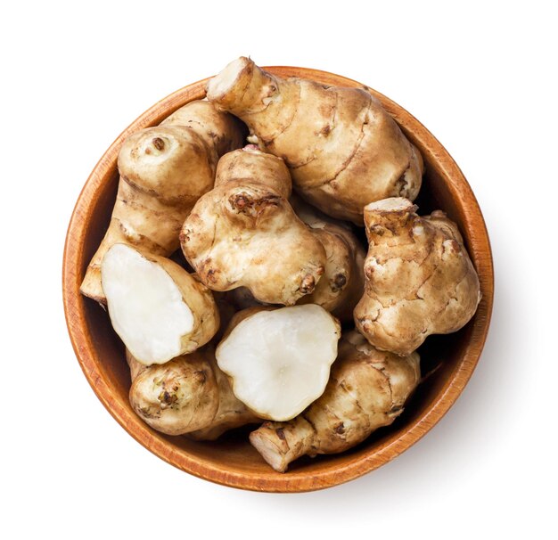 Jerusalem artichoke and half in a wooden plate on a white background Top view