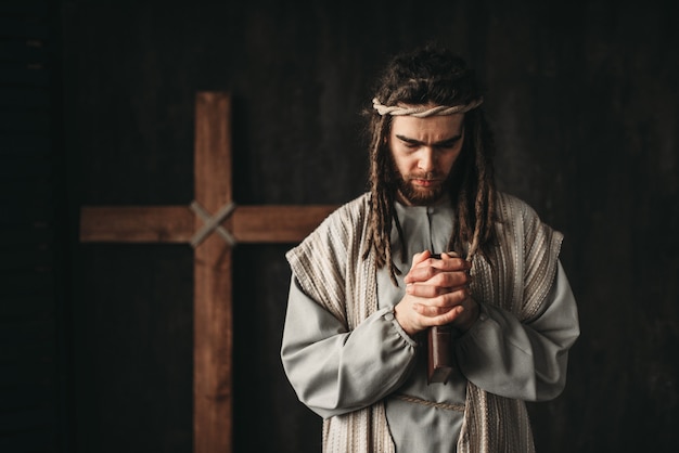 Jesus Christ praying with bible in hands, cross on black