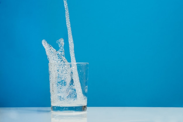 Photo jet of splash water filling a glass on blue background. with copyspace