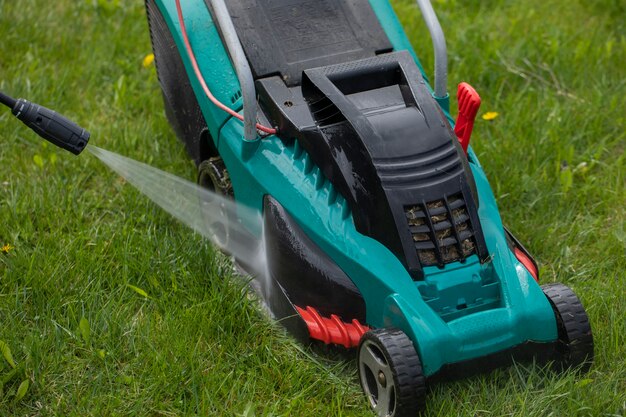 Jet of water from high-pressure washer cleans lawn mower on green grass