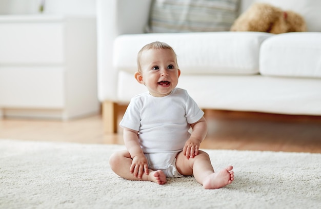 jeugd, babytijd en mensenconcept - gelukkige kleine babyjongen of meisje zittend op de vloer thuis