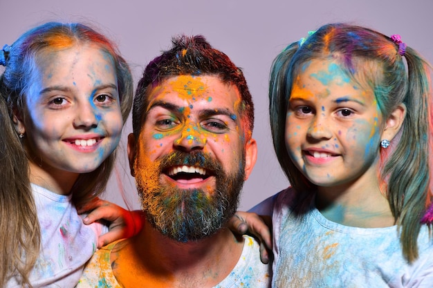 Foto jeugd- en vakantieconcept schoolmeisjes en man met baard hebben verfvlekken op gezichten meisjes en jongen met blije gezichten staan op paarse achtergrond kinderen met paardenstaarten staan dicht