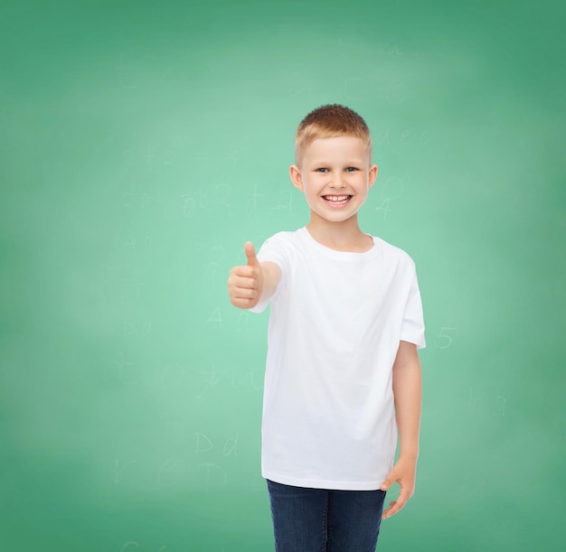 jeugd, gebaar, onderwijs, reclame en mensen concept - lachende jongen in wit t-shirt duimen opdagen over groene bord achtergrond