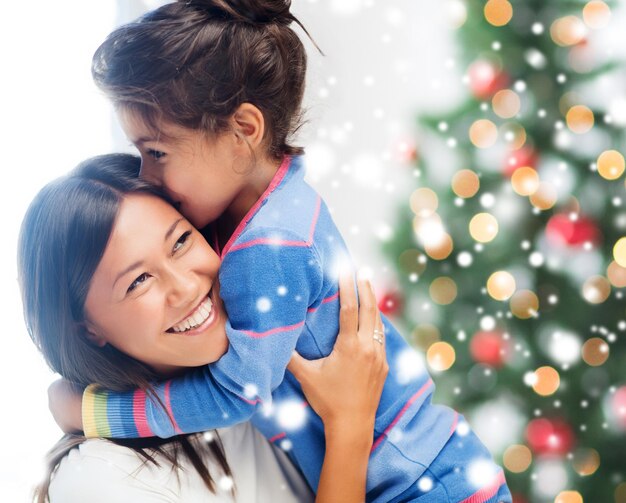 jeugd, geluk, kerst, familie en mensen concept - glimlachend klein meisje en moeder knuffelen binnenshuis