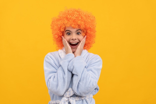 Jeugd geluk. verjaardags- of pyjamafeestje. grappige jongen in krullende clown pruik. mooie kinderbadjas voor thuis. verrast tienermeisje met oranje haar in gezellige nachtkleding. Goedemorgen.