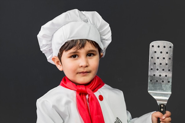 Jeugd, kleine jongen die gezond voedsel op de keuken bereidt over een grijze achtergrond, kook hoed