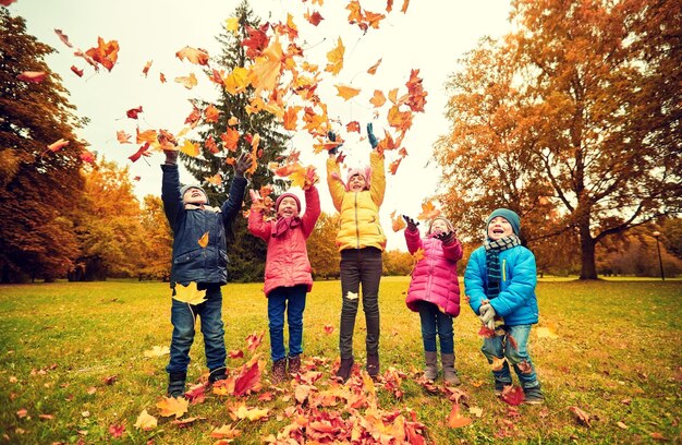 jeugd, vrije tijd, vriendschap en mensen concept - groep gelukkige kinderen spelen met herfst esdoorn bladeren en plezier in het park