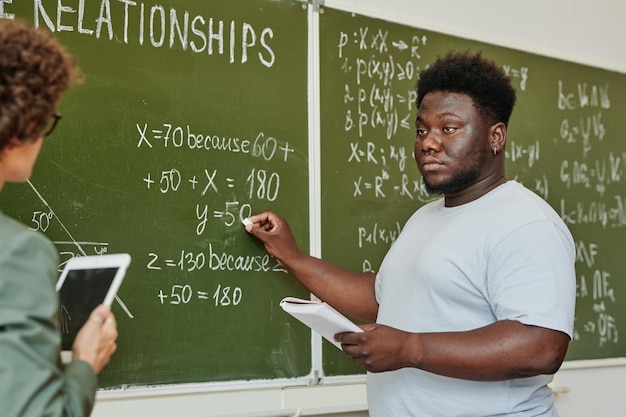 Jeugdige student wijzend op bord tijdens uitleg van vergelijking