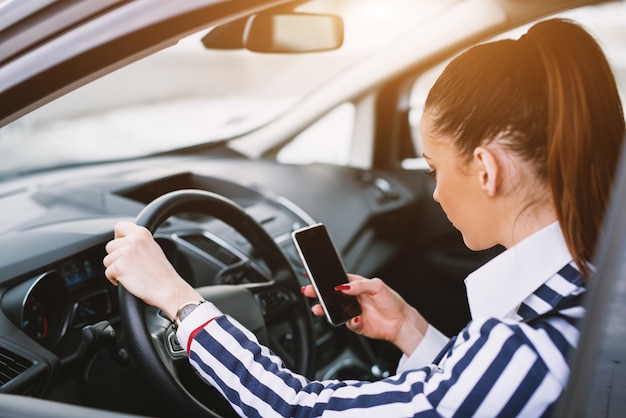 Jeugdige vrouw die van haar celtelefoon texting terwijl het zitten in de auto.