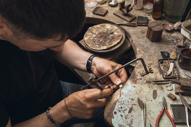 Foto un gioielliere sega un piccolo pezzo di metallo per riparare un anello d'oro nel suo laboratorio