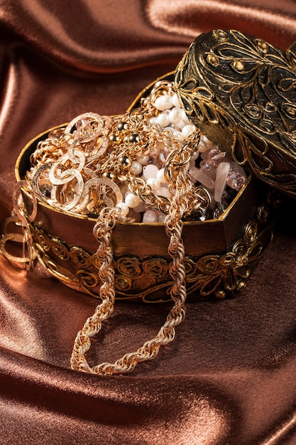 Бижутерия и другие украшения в декоративной шкатулке в форме сердца на шелковой ткани.