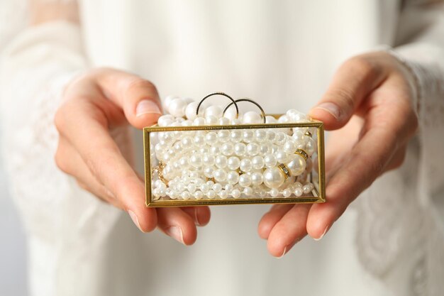 Jewelry box with pearls and wedding rings in female hands on light background