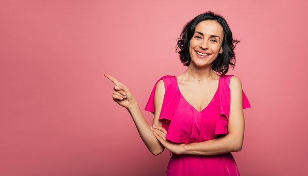 Jewelry. Close-up photo of a lady in a purple dress and a golden necklace, who is looking in the camera and pointing to the right with her right hand.