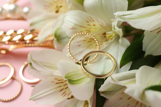 Jewelry and flowers on pink background, close up