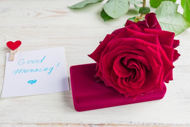 jewelry gift box and bautiful red rose on wooden background Whishing good morning on white piece of paper