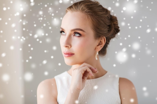 jewelry, luxury, christmas, holidays and people concept - beautiful woman in white dress with diamond earring over snow