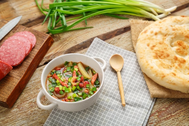 Zuppa di fagioli della cucina ebraica cholit su un tovagliolo grigio accanto a salsiccia di cipolle verdi e focaccia