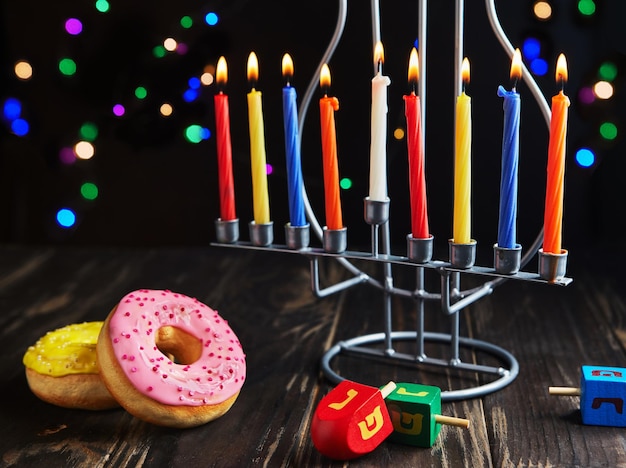 Photo jewish holiday hanukkah background a traditional dish is sweet donuts hanukkah table setting candlestick with candles and spinning tops on black background lighting chanukah candles copy space