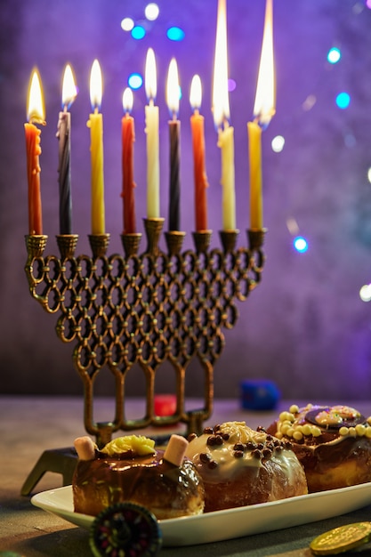 Festa ebraica hanukkah sfondo. un piatto tradizionale sono le ciambelle dolci. hanukkah tavolo impostazione di un candeliere con candele e trottole su un blu illuminazione candele chanukah