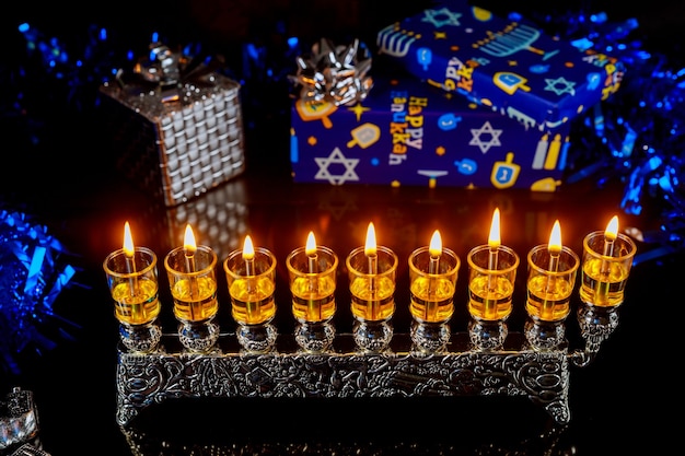 Photo jewish holiday hanukkah background with burning menorah and gift boxes.