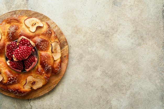 ユダヤ教の祝日ロシュ・ハシャナまたはロシュ・ハシャナザクロリンゴ蜂蜜と素朴な灰色のテーブル背景に丸いチャラーユダヤ人の秋のお祝いシャナ・トヴァ・ヨム・キプールのコンセプトトップビュー
