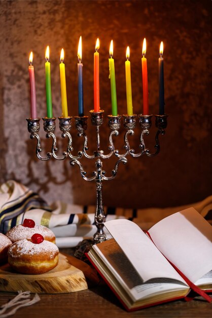 Jewish religious holiday Hanukkah with holiday Hanukkah traditional candelabra doughnut on a dark background and Religious books Tanakh