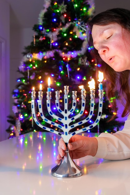 Jewish woman blows out the candles on Hanukkah menorah with nine candles