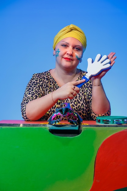 A jewish woman in a headdress with a magen david painted face directs the noise on purim while