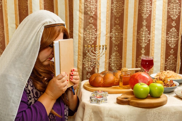 A Jewish woman in a headscarf that falls from her hair holds a siddur to her face after the holiday prayer for Shabbat and Rosh Hashanah