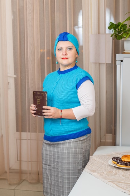 Еврейская женщина в головном уборе кисуй рош стоит у стола, на котором стоят пончики на Хануку, и держит в руках книгу Тегилим с надписью на русском и иврите.