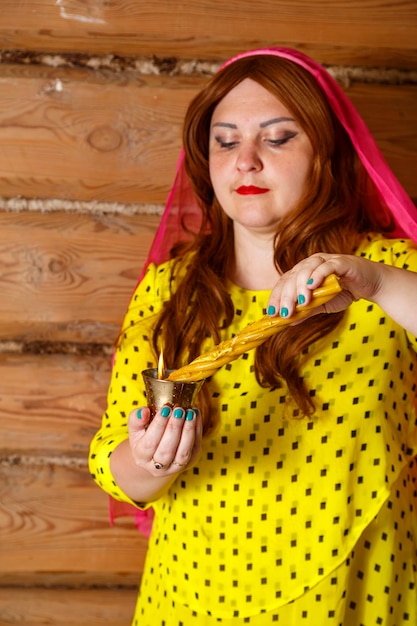 A Jewish woman in a wig and a flowing headscarf makes Avdalah with candles and a glass of wine