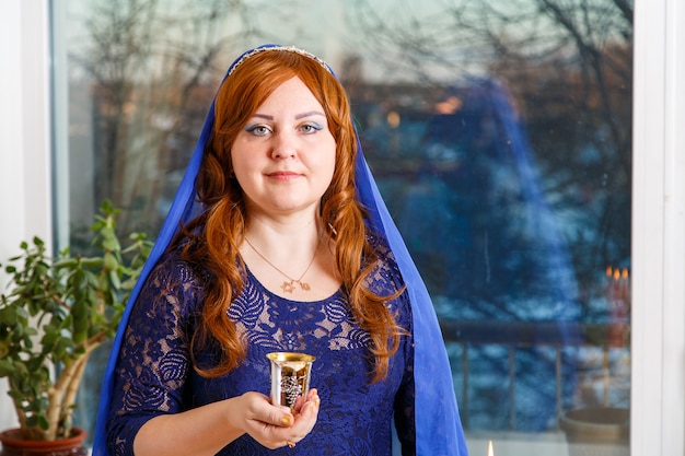 Photo a jewish woman with her head covered in a blue cape at the passover seder table makes kiddush for wine