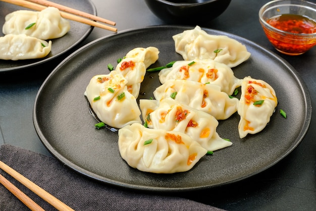 Photo jiaozi gyoza dumplings steamed on black plates with soy sauce and chili oil.