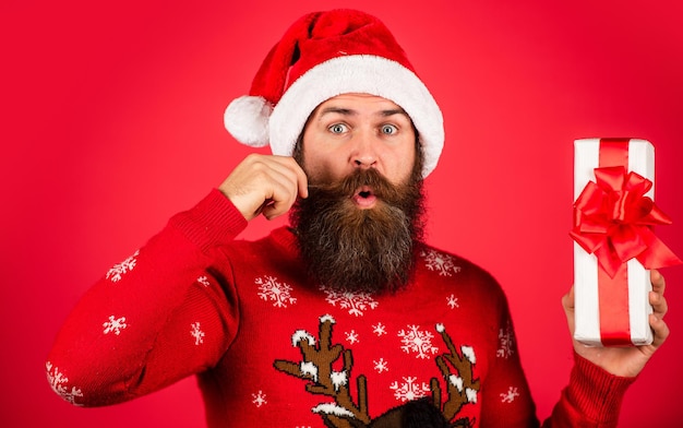 Jingle bells. winter holiday party. mature guy celebrate new year. bearded hipster in xmas sweater. surprised man with beard in santa claus hat. brutal man hold present box. christmas online shopping.