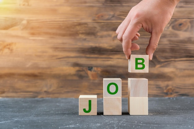 РАБОТА. Концепция поиска работы, мужская рука опускает деревянный куб с буквой B, образующей слово JOB