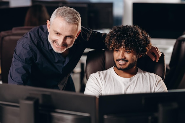 Photo job mentor checking new employee task smiling supervisor and trainee guy looking at monitor in office