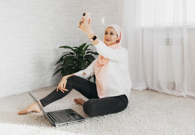 이슬람 여성 개념을 위한 직업 기회. 집에서 바닥에 앉아 전화 통화 하는 hijab에 웃는 소녀.