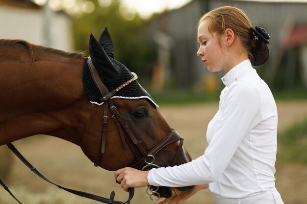 jockey female rider portrait in white uniform holds bridle of dressage horse at stable