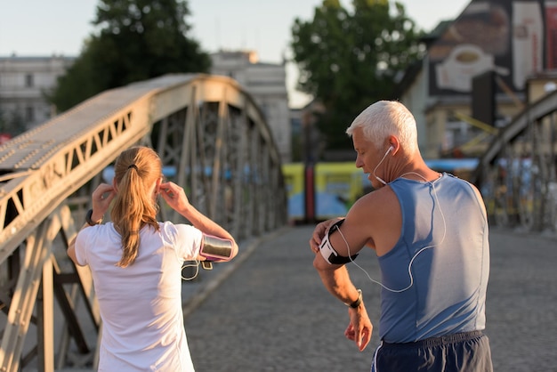 joggend koppel controleer de muziekafspeellijst op de telefoon en plan de route voor de ochtendtraining met zonsopgang in de stad en zonnevlam op de achtergrond