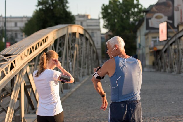 joggend koppel controleer de muziekafspeellijst op de telefoon en plan de route voor de ochtendtraining met zonsopgang in de stad en zonnevlam op de achtergrond