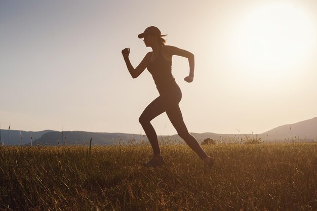 Joggende vrouw die in de zomerveld loopt bij zonsondergang