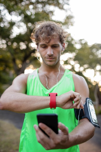 Jogger listening to music on mobile phone and checking his smartwatch