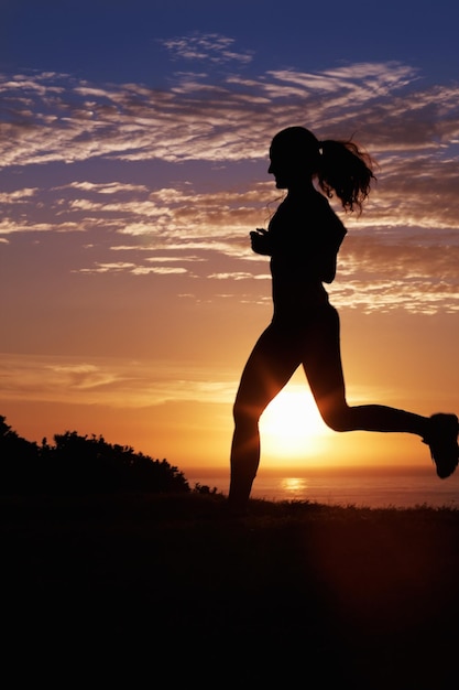 Jogging at sunrise Silhouette of a woman listening to music and running by the sea at sunrise