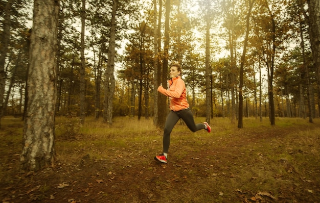 Jogging through the autumn forest. Young fit woman in sportswear runs along forest path. Healthy lifestyle concept