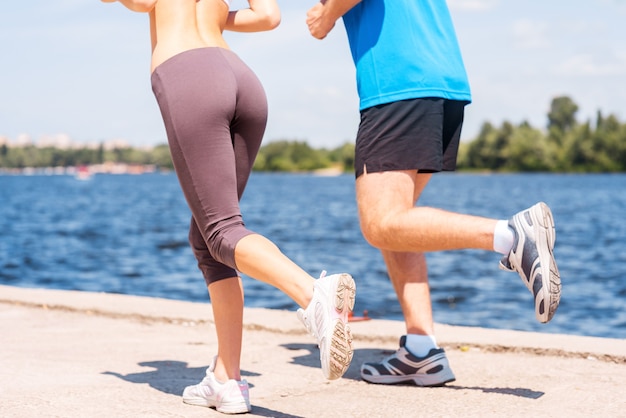 Jogging together.  Close-up of young woman and man in sports clothing running along the riverbank
