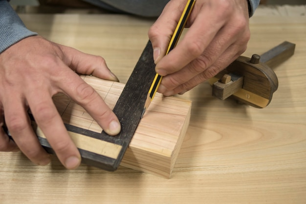 A joiner with a pencil and a square marks the workpiece