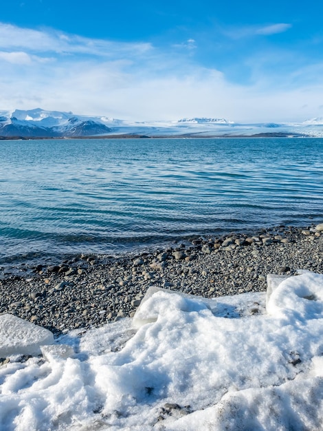 写真 アイスランドの曇った青い空の下に氷河と大きな氷山があるヨークルスアゥルロゥン氷山ラグーン