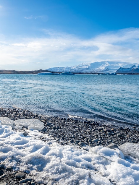 Jokulsarlon iceberg lagoon with glacier and large iceberg under cloudy blue sky in Iceland