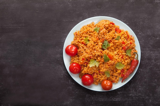 Pomodori di riso jollof e peperoncino su un piatto blu cucchiaio a forchetta su un tovagliolo di lino su sfondo nero cucina nazionale dell'africa